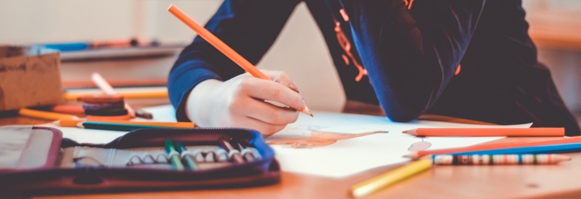 Symbolbild Schule: Schülerin sitzt am Tisch mit Heften und Stiften
